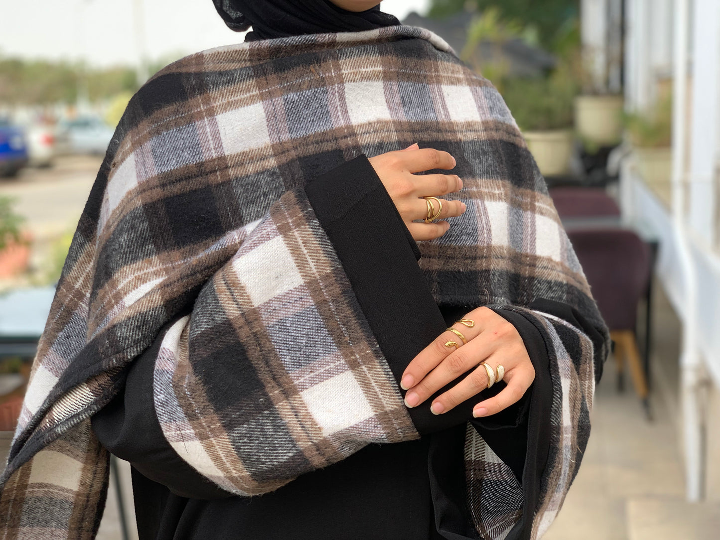 Person wearing a black abaya and plaid shawl with a blurred outdoor background